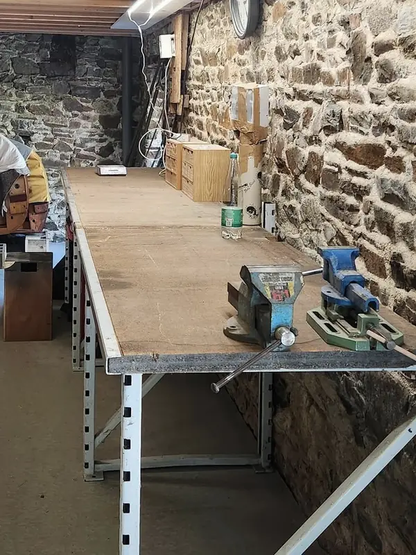 Établi de l'atelier, étau et serre-joint devant un mur en pierre