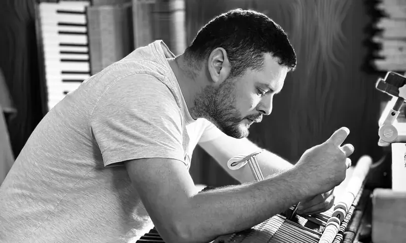 Geoffroy Szirmay penché sur la mécanique d'un piano, dans son atelier