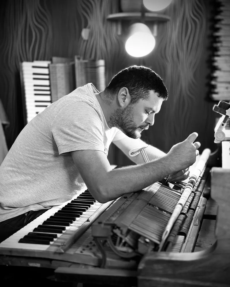 Geoffroy Szirmay penché sur la mécanique d'un piano, dans son atelier